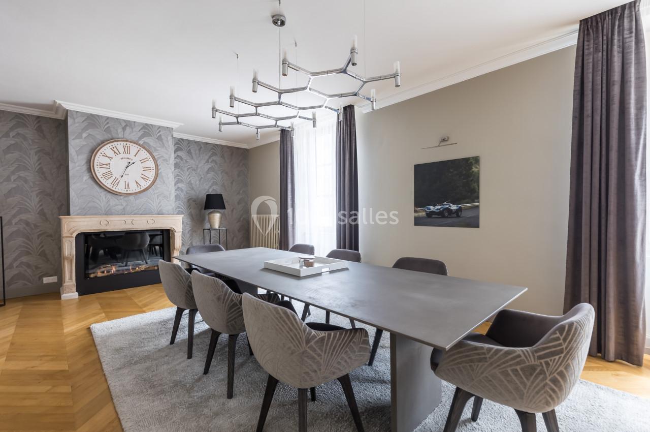 Salle à manger moderne avec table en métal, chaises grises, cheminée, horloge murale et tableau décoratif.