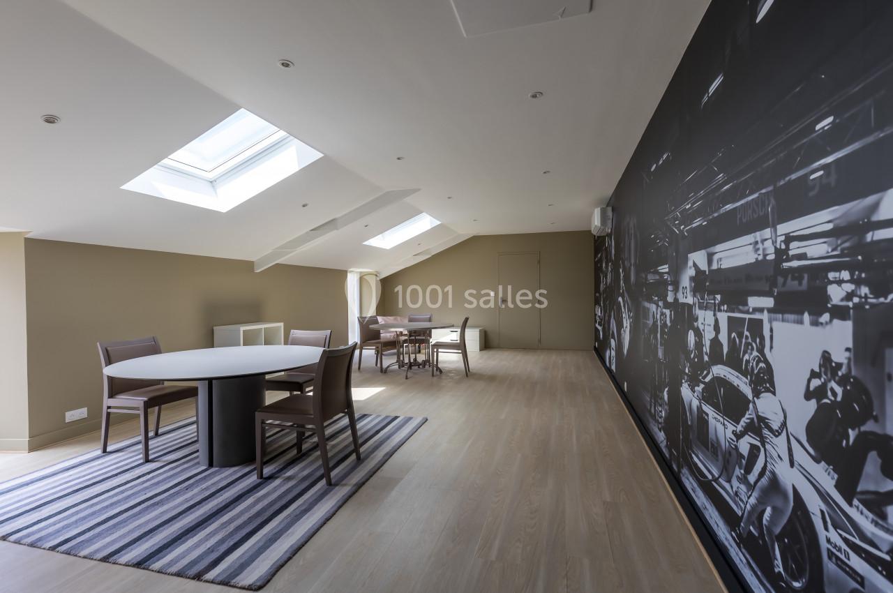 Salle lumineuse sous combles avec table ronde, chaises, tapis rayé et mur décoré d'une fresque en noir et blanc.