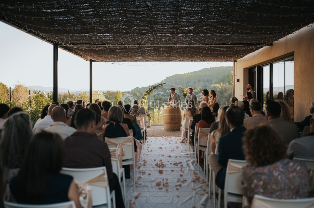 Cérémonie de mariage en plein air sous une pergola, avec des invités assis et un couple devant un officiant.