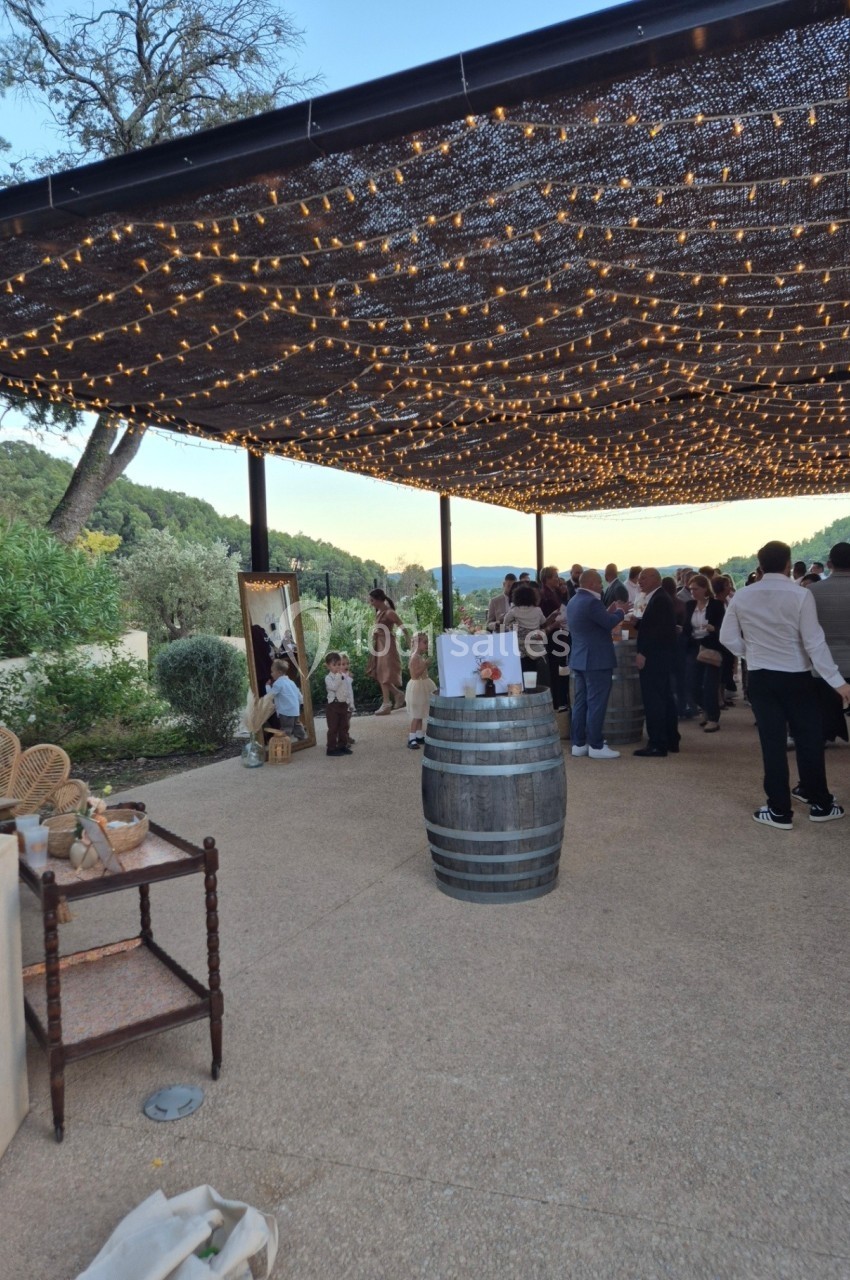 Groupe de personnes rassemblées sous une pergola illuminée, entourées de décorations et d'un paysage naturel.