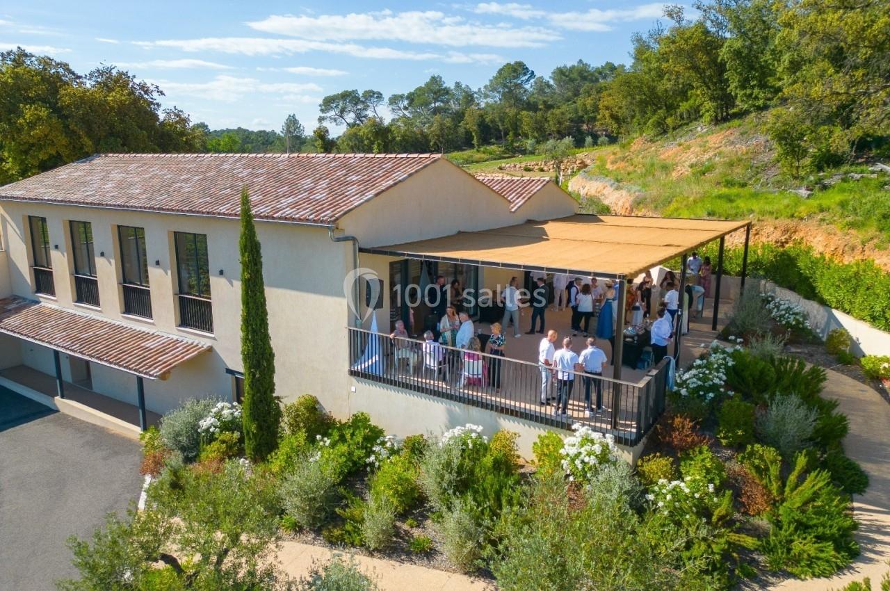 Vue aérienne d'un bâtiment avec une terrasse ombragée où des personnes sont rassemblées, entouré de végétation.