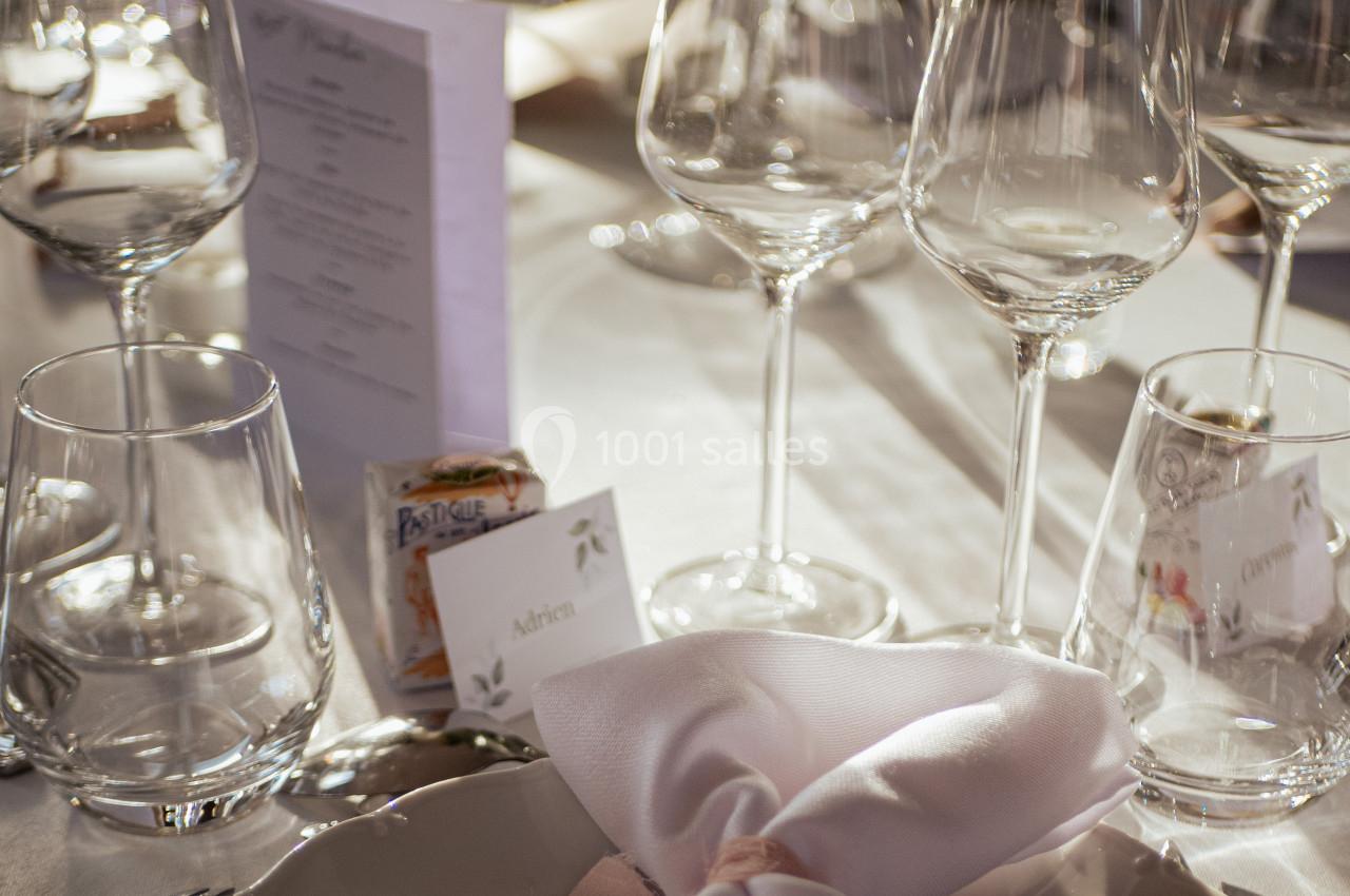 Table dressée avec des verres à vin, un menu, un marque-place et une serviette pliée sur une assiette.