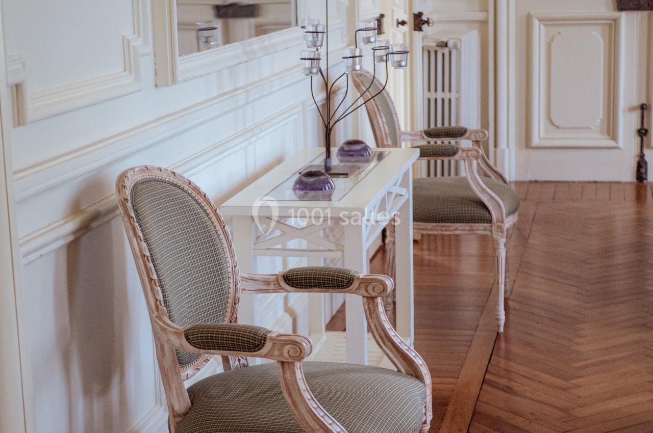 Deux fauteuils anciens encadrent une console blanche ornée de bougeoirs et de décorations violettes dans une pièce élégante.