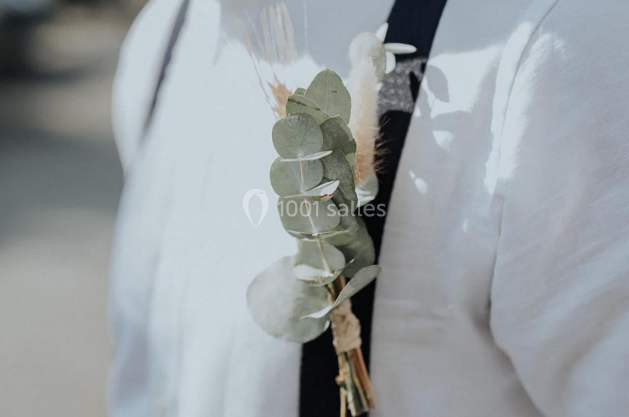 Branche d'eucalyptus et fleurs séchées attachées à une bretelle noire sur une chemise blanche.