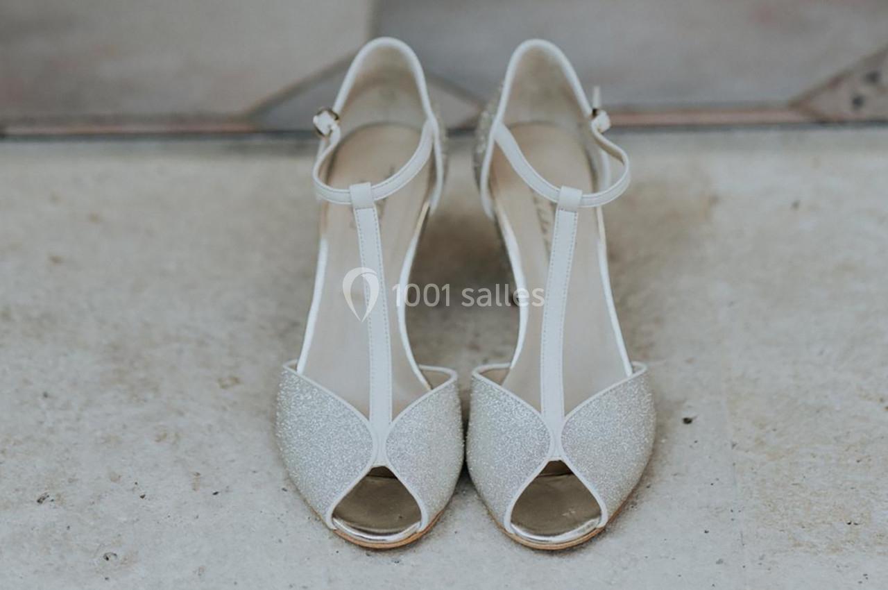 Chaussures à talons ouvertes en T, blanches et pailletées, posées sur un sol en pierre beige.