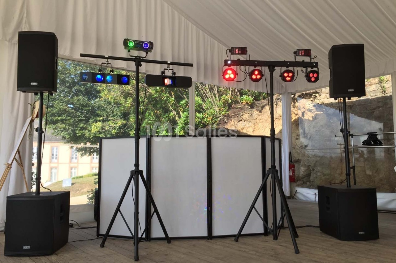 Installation de matériel de sonorisation et d'éclairage sous une tente, avec haut-parleurs et projecteurs colorés.