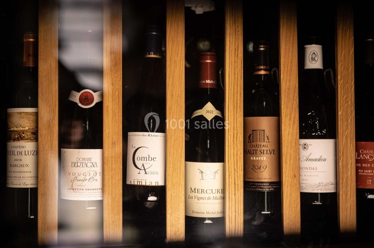 Bouteilles de vin rouge et blanc alignées verticalement dans une étagère en bois éclairée.