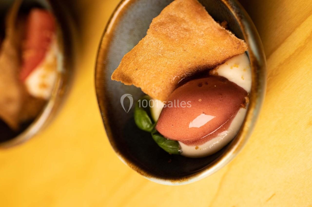 Dessert dans un bol en céramique avec une boule de glace, une crème blanche, un biscuit et des feuilles vertes.