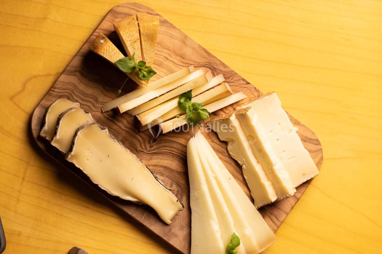 Plateau en bois avec une variété de fromages tranchés, décoré de feuilles de basilic, posé sur une table jaune.