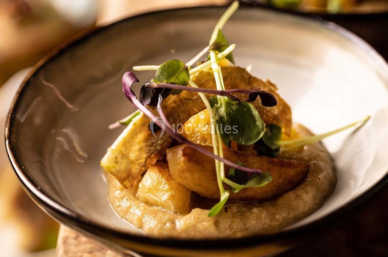 Assiette contenant un plat composé de morceaux de légumes rôtis, purée et jeunes pousses en garniture.