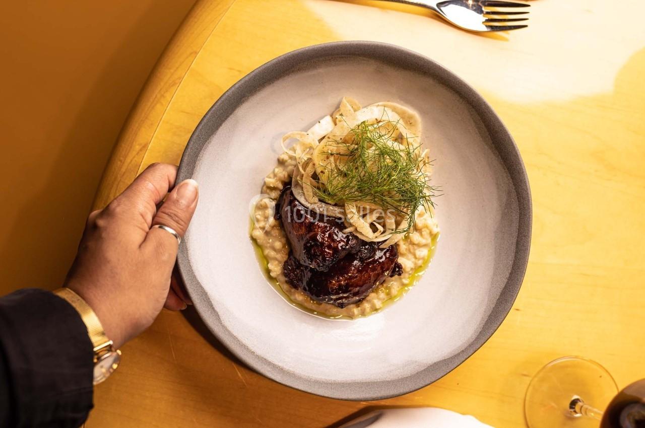 Assiette de viande braisée servie sur un lit de risotto crémeux, garnie de fenouil et d'herbes fraîches.