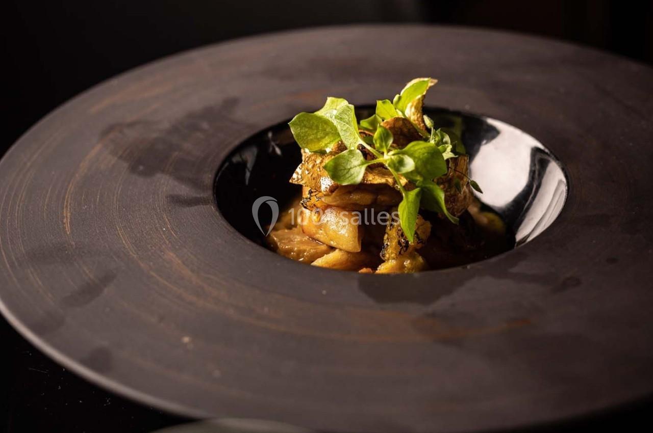 Assiette gastronomique avec des légumes racines caramélisés, garnis de jeunes pousses, présentée sur une assiette noire.
