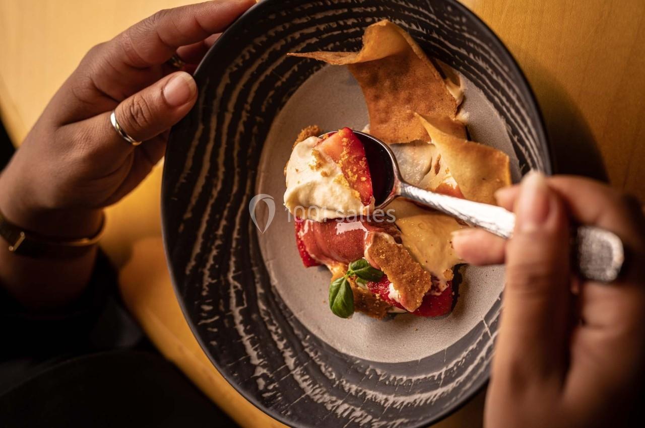 Personne dégustant un dessert composé de fruits rouges, crème et tuiles croustillantes dans une assiette sombre.