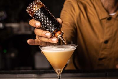 Miniature Location salle Paris 19 (Paris) - L'Envol de la Philharmonie #61 Un barman verse un liquide sombre dans un verre à cocktail rempli d'une boisson mousseuse.