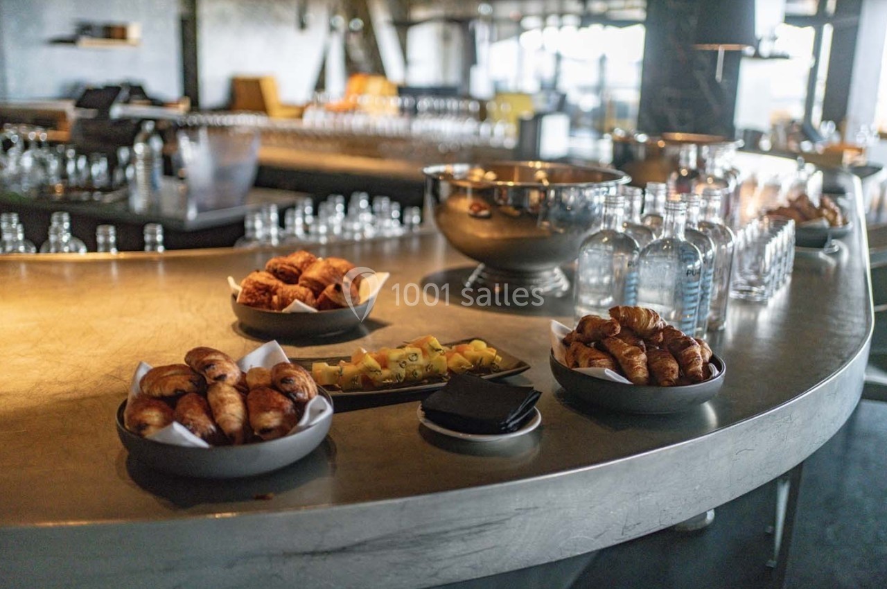 Assortiment de viennoiseries et fruits frais disposés sur un comptoir en métal dans un espace lumineux.