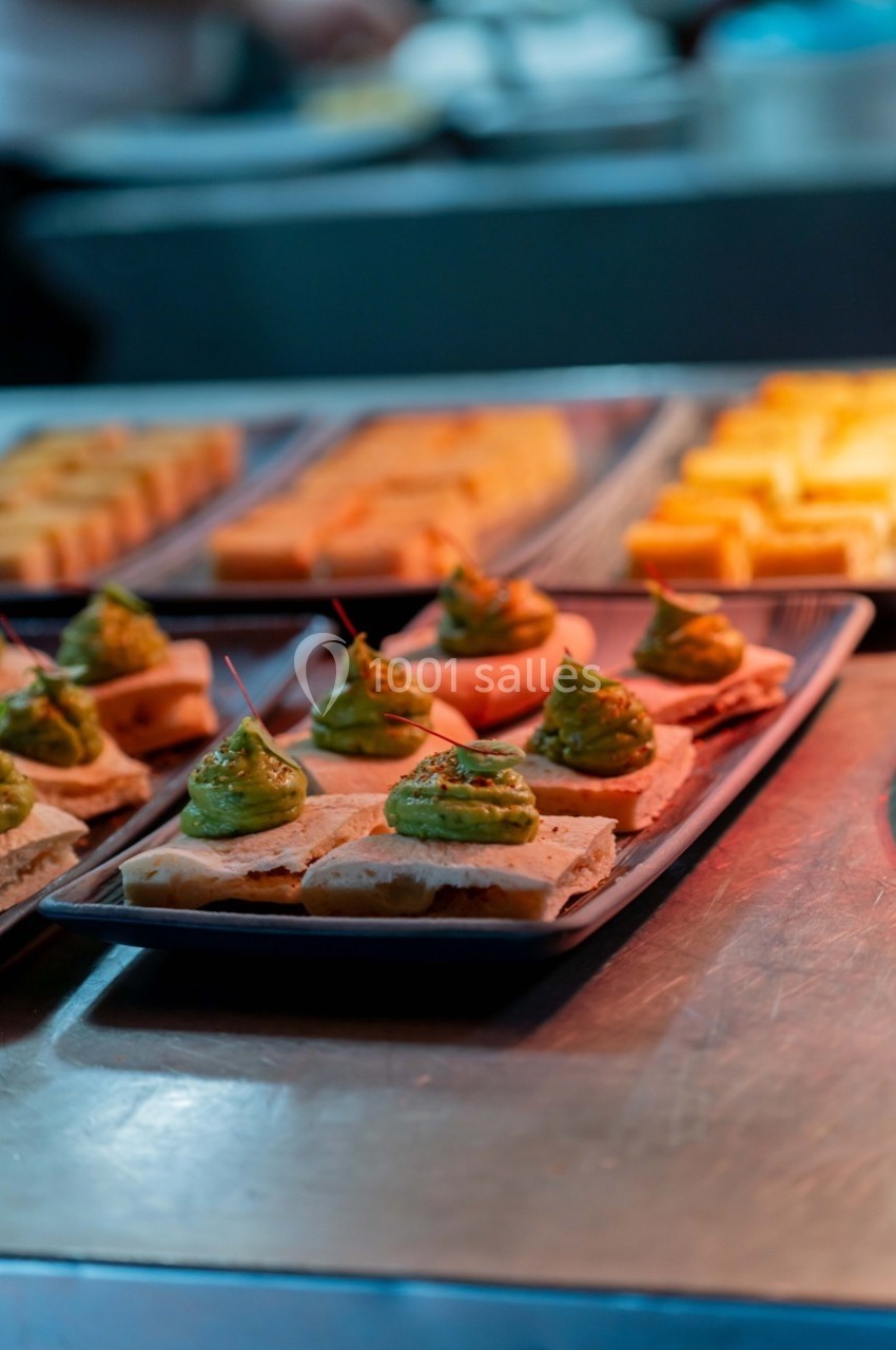Assiette de toasts garnis de crème verte, disposés sur un comptoir en métal avec d'autres plats en arrière-plan.