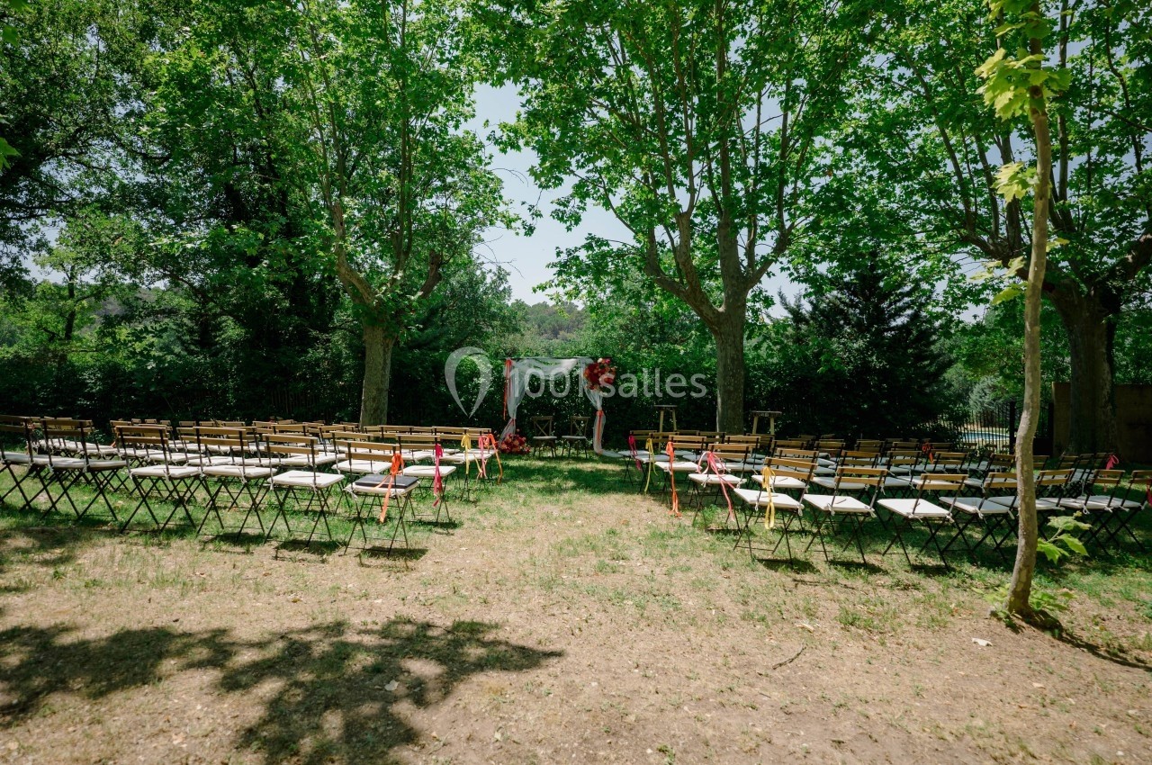 Chaises disposées en rangées dans un jardin verdoyant, face à une arche décorée pour une cérémonie en plein air.