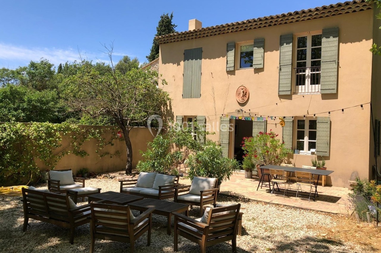 Maison provençale avec volets verts, terrasse aménagée avec salon de jardin et table, entourée de végétation.
