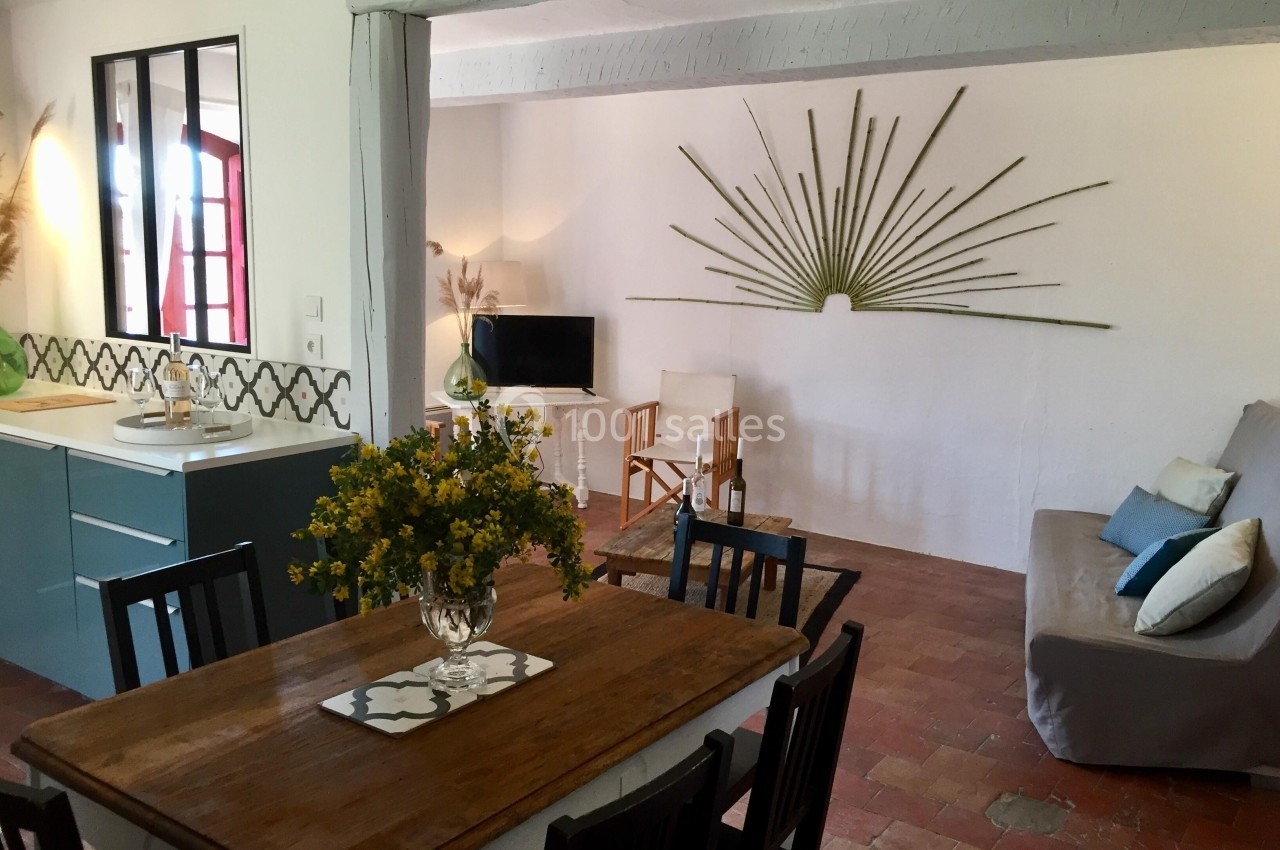 Salle de séjour lumineuse avec table en bois, canapé, télévision, cuisine ouverte et décoration murale en branches.