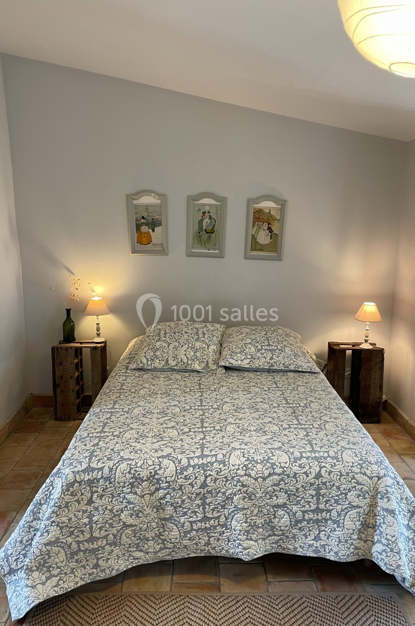 Lit double avec couvre-lit à motifs, encadré par deux tables de chevet en bois avec lampes, dans une chambre lumineuse.