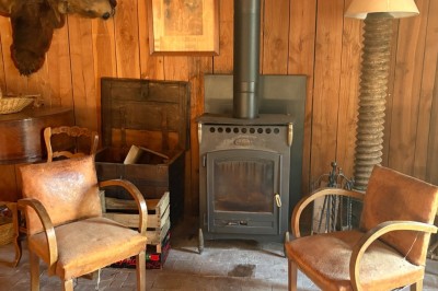 Deux fauteuils en cuir disposés près d'un poêle à bois dans une pièce au mur en bois décorée de cadres et d'une tête d'ours.