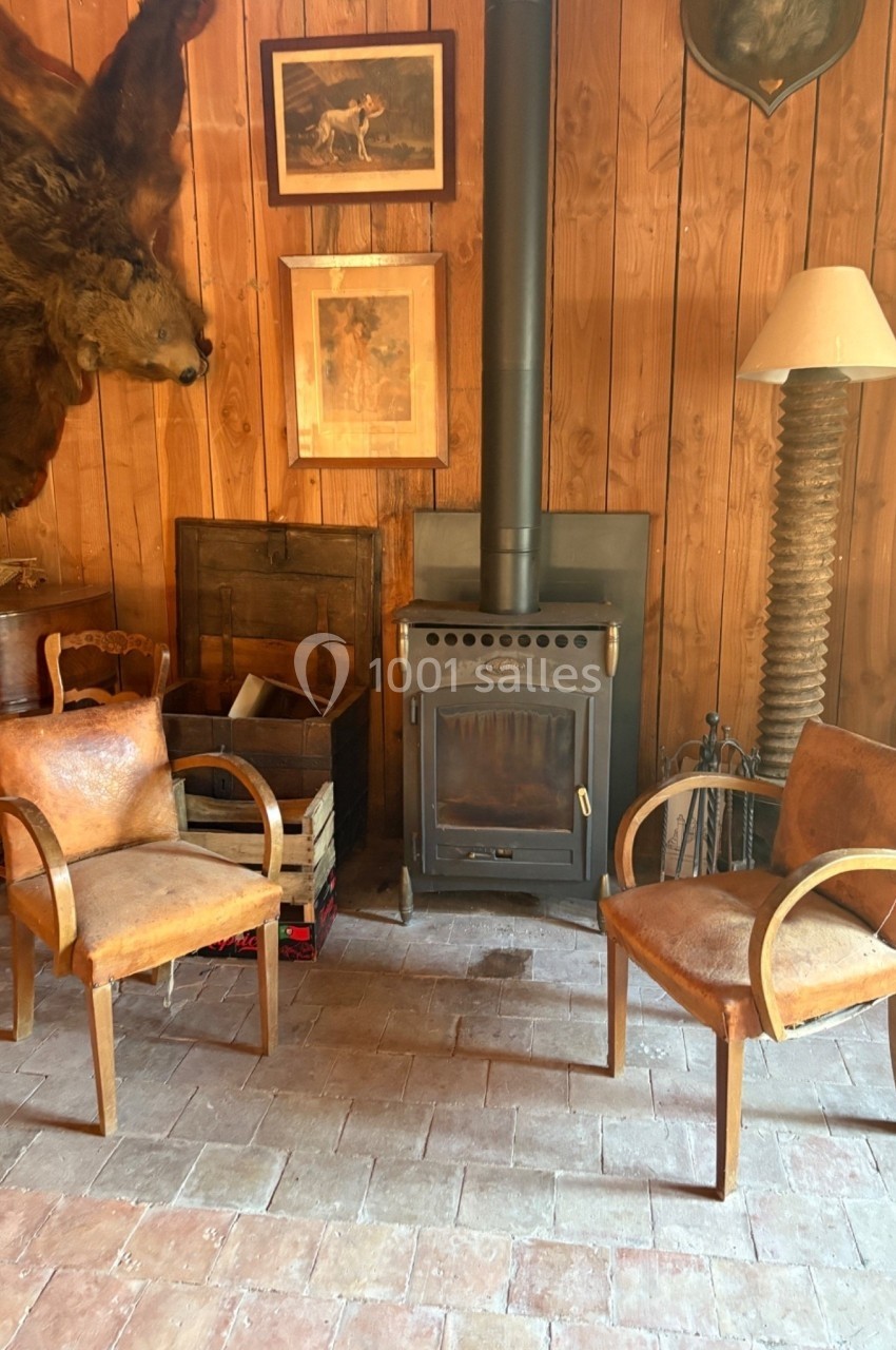 Deux fauteuils en cuir disposés près d'un poêle à bois dans une pièce au mur en bois décorée de cadres et d'une tête d'ours.