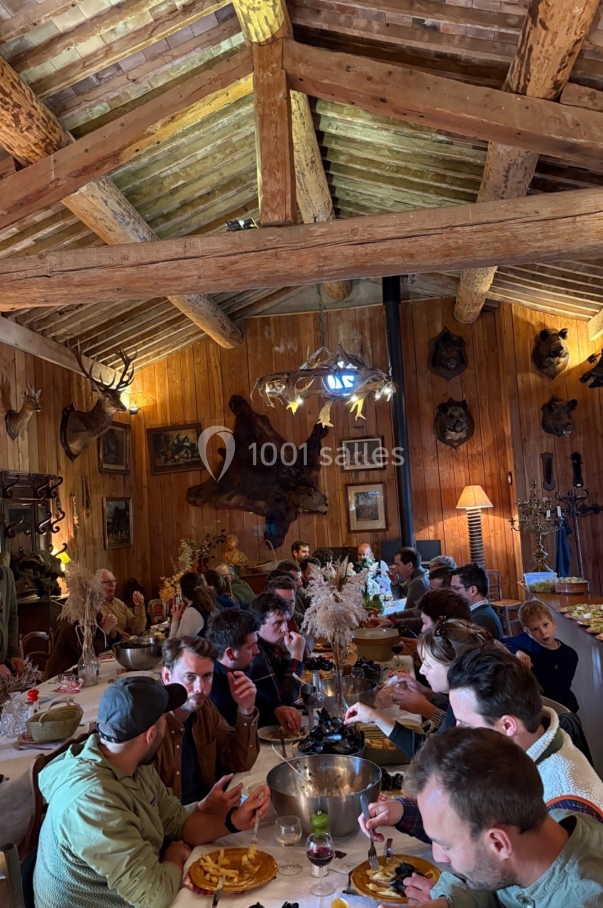 Des convives partagent un repas dans une salle rustique avec des murs en bois et des décorations de chasse.