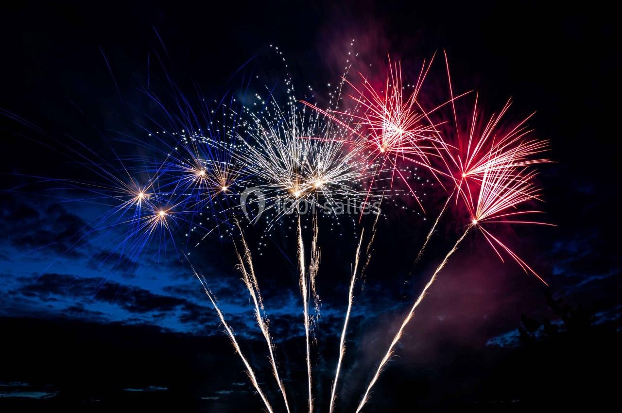 Feux d'artifice multicolores illuminant un ciel nocturne avec des traînées lumineuses.