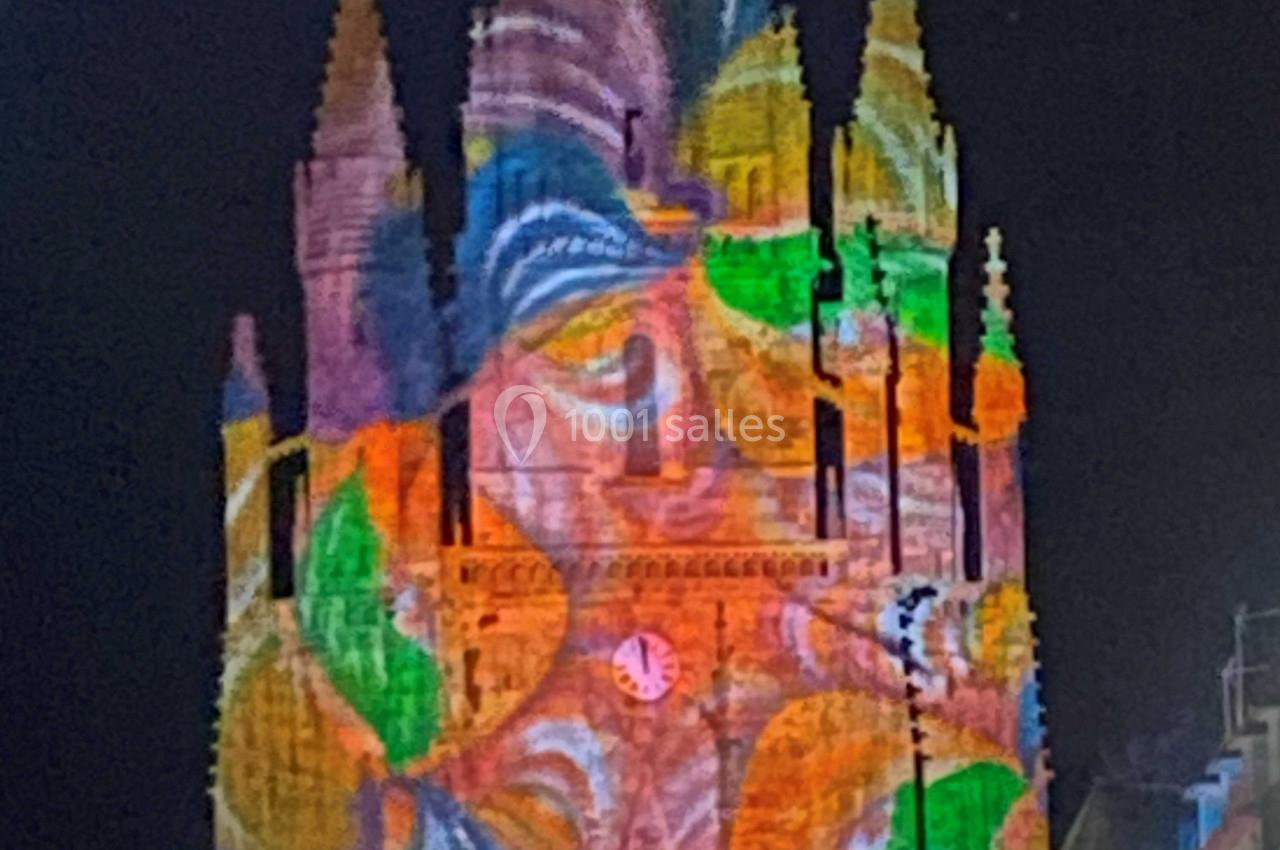 Projection lumineuse colorée représentant un visage sur la façade d'une église gothique de nuit.