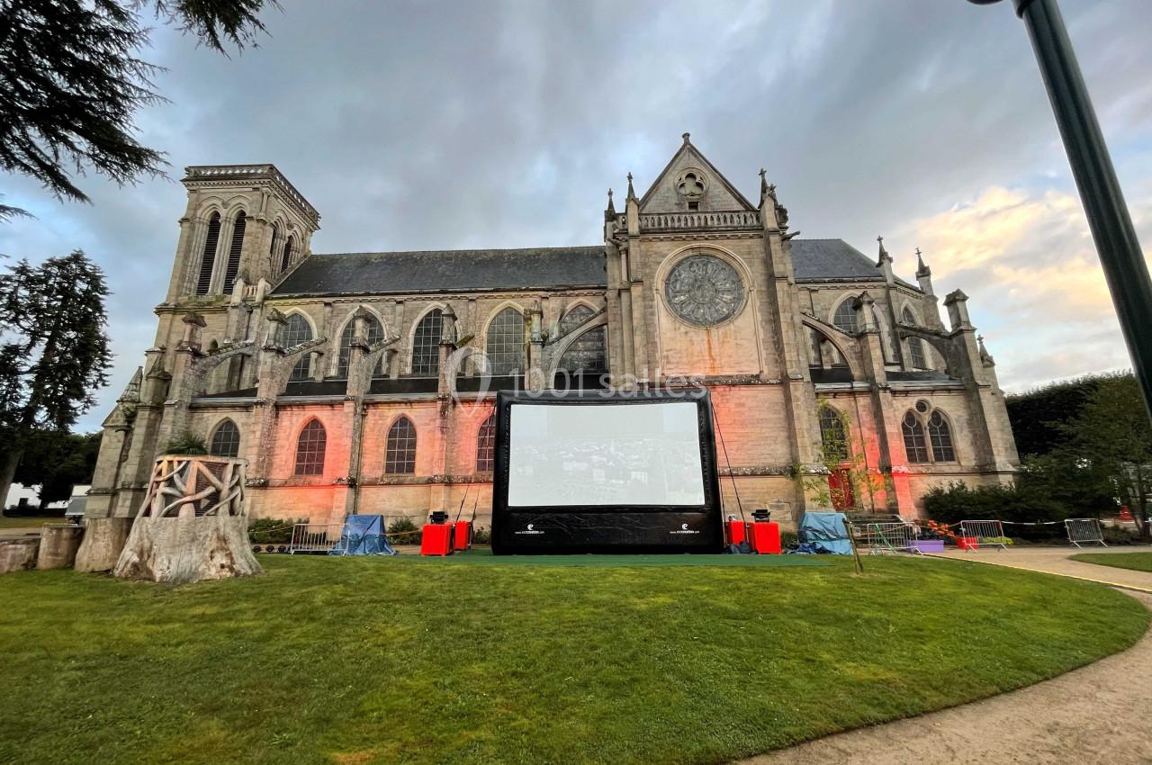 Écran de projection installé sur une pelouse devant une église gothique éclairée à la tombée du jour.