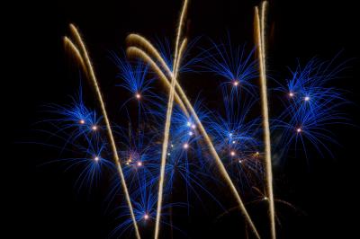 Feux d'artifice avec des traînées dorées et des éclats bleus sur un fond de nuit noire.