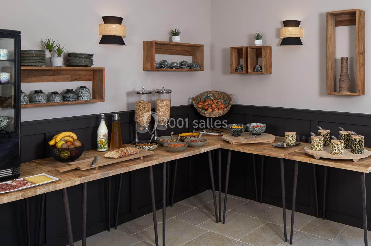 Buffet de petit-déjeuner avec céréales, fruits, viennoiseries et boissons, disposé sur des tables en bois dans une salle…
