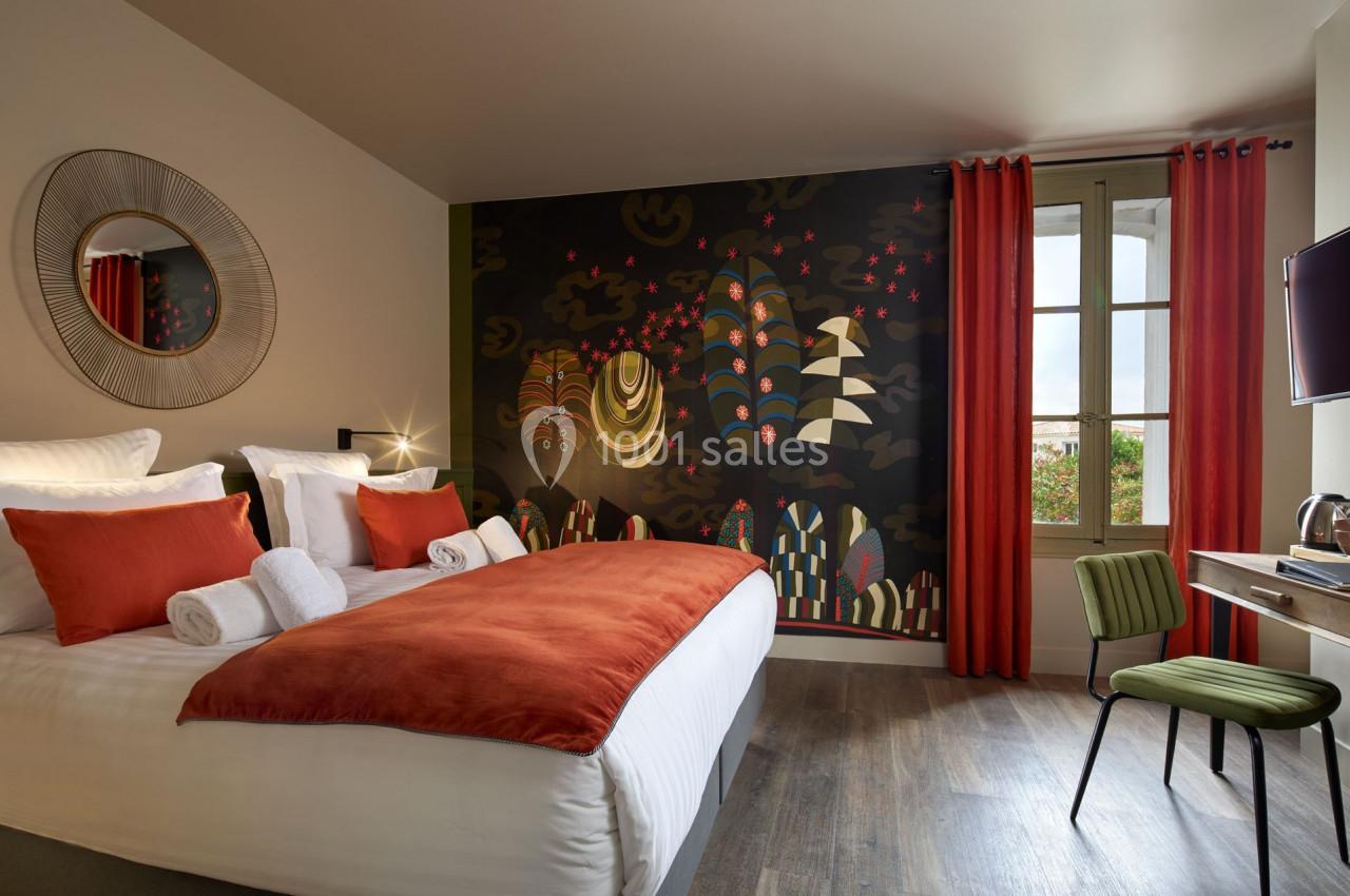 Chambre moderne avec lit double, tête de lit décorée d'une fresque colorée, fenêtre et bureau avec chaise verte.