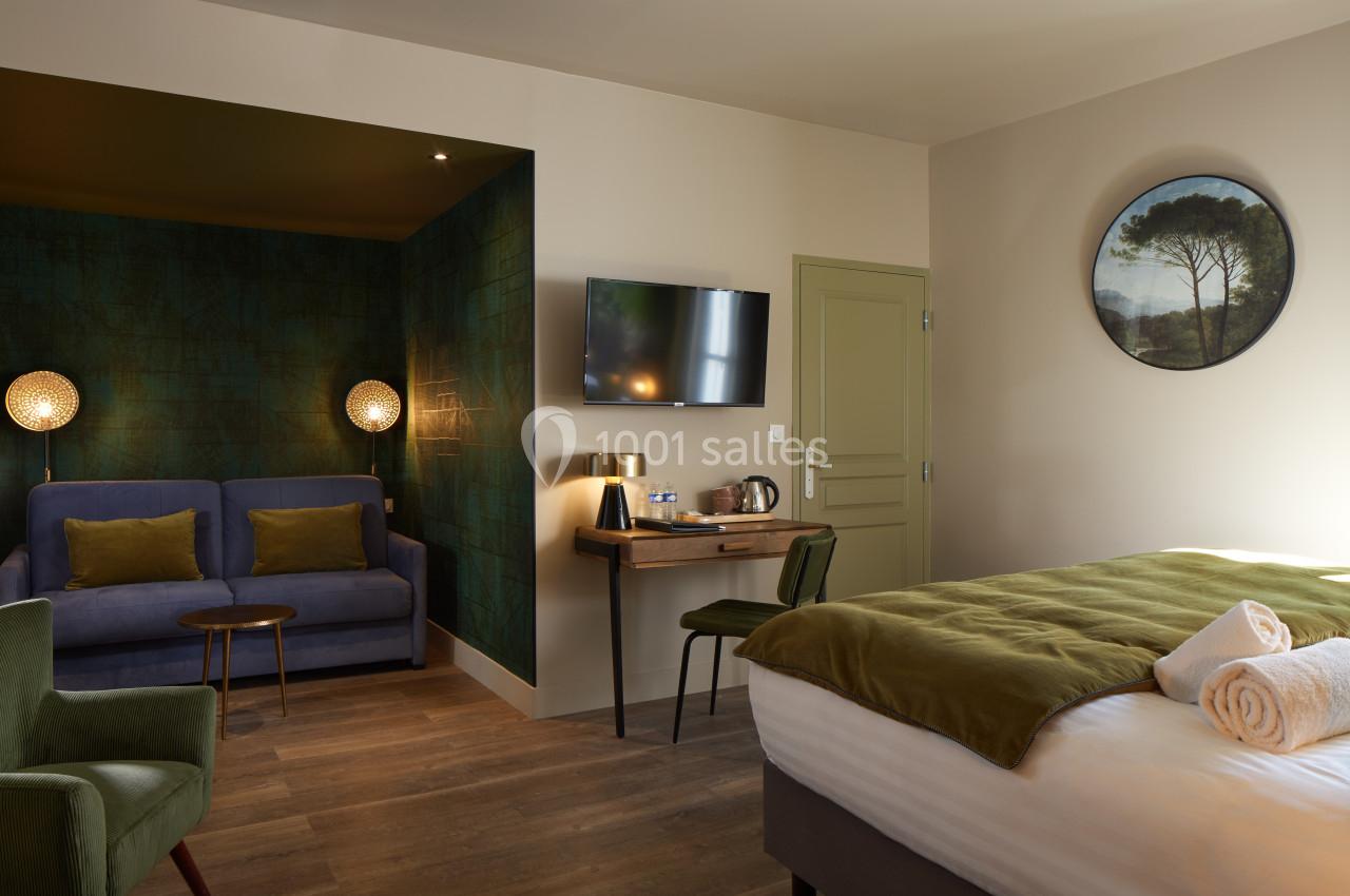 Chambre d'hôtel avec lit double, canapé, bureau, télévision murale et éclairage tamisé dans une ambiance chaleureuse.