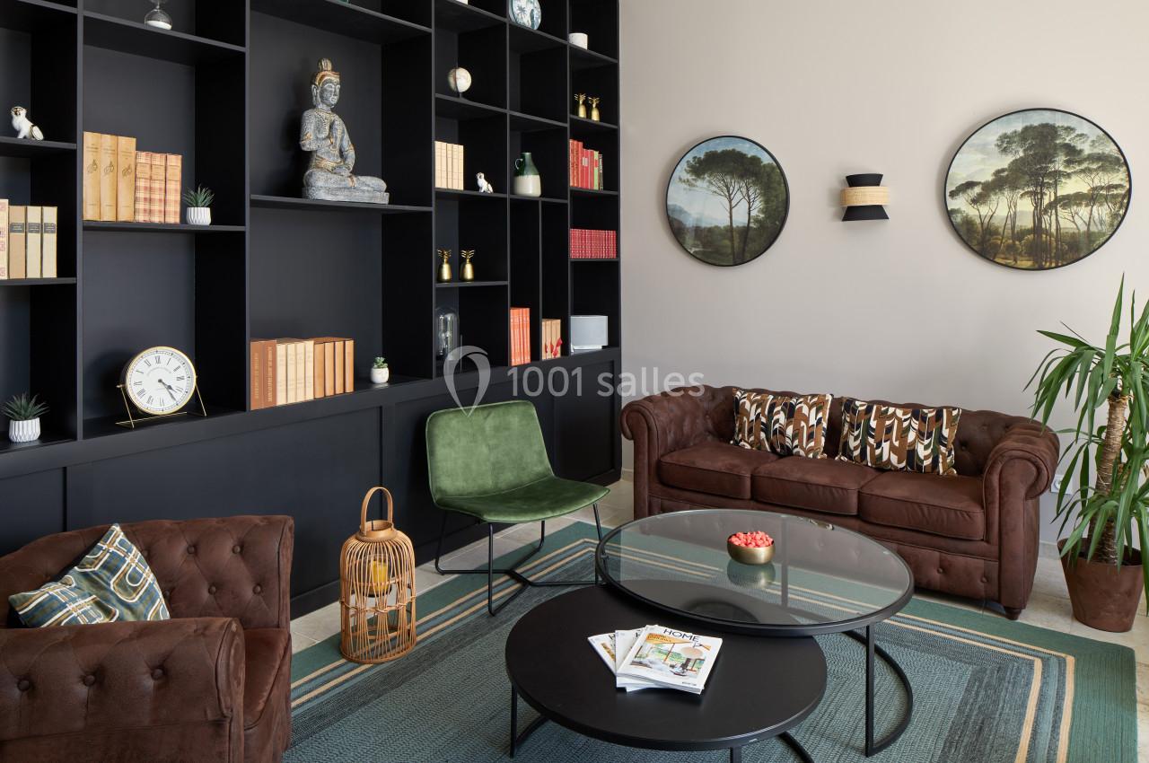 Salon moderne avec canapé en cuir, étagères noires remplies de livres et décorations, table basse ronde et plantes.