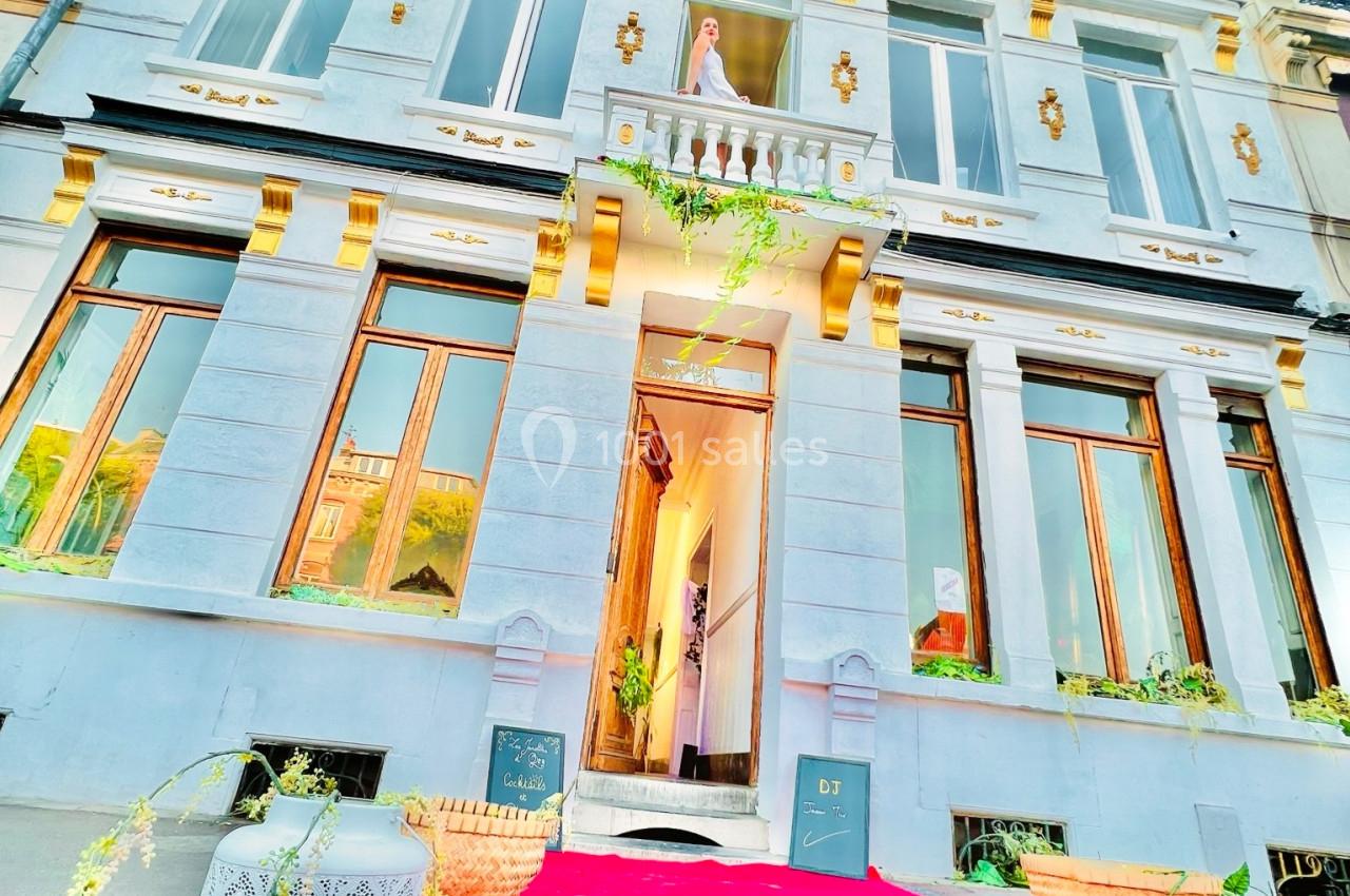 Façade d'un bâtiment élégant avec balcon, tapis rouge à l'entrée et décorations végétales.