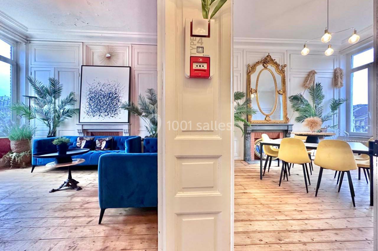 Intérieur lumineux avec salon bleu à gauche, salle à manger avec miroir doré à droite, et plantes décoratives.