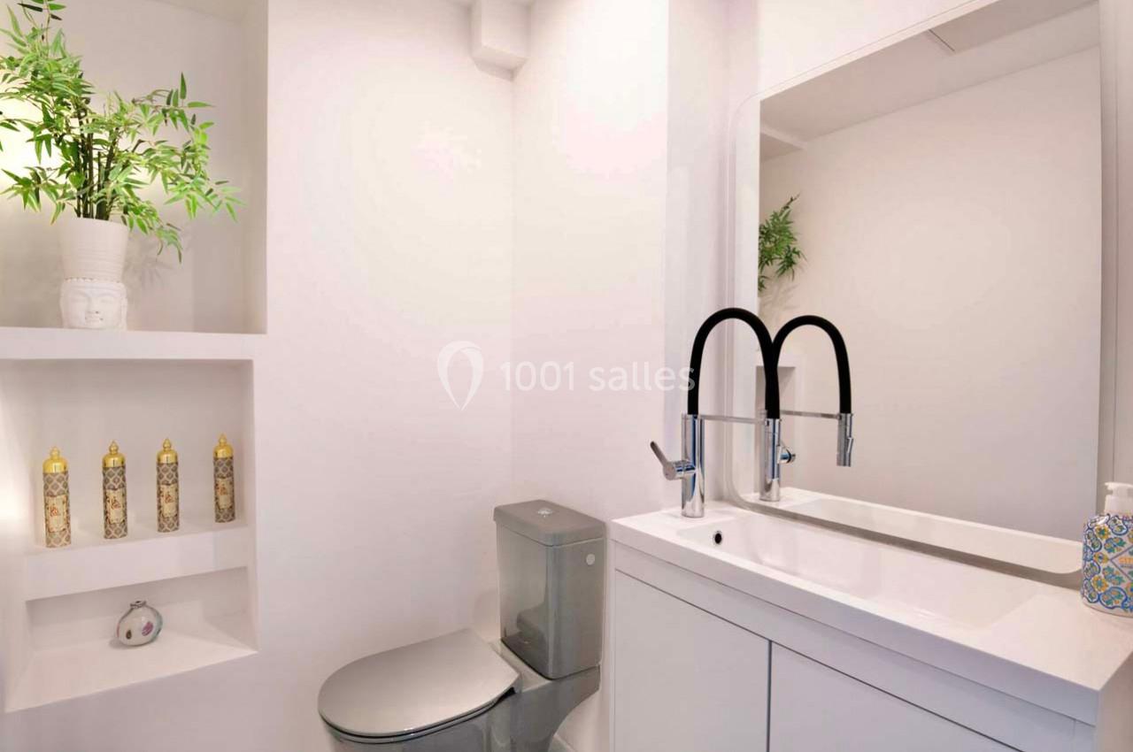 Salle de bain moderne avec lavabo double, miroir, toilettes grises et étagères décorées de plantes et flacons.