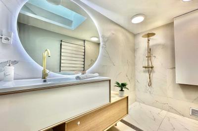 Salle de bain moderne avec lavabo double, miroir, toilettes grises et étagères décorées de plantes et flacons.