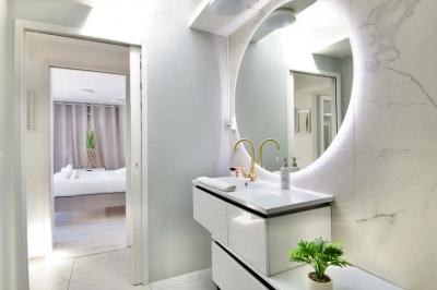 Salle de bain moderne avec lavabo double, miroir, toilettes grises et étagères décorées de plantes et flacons.
