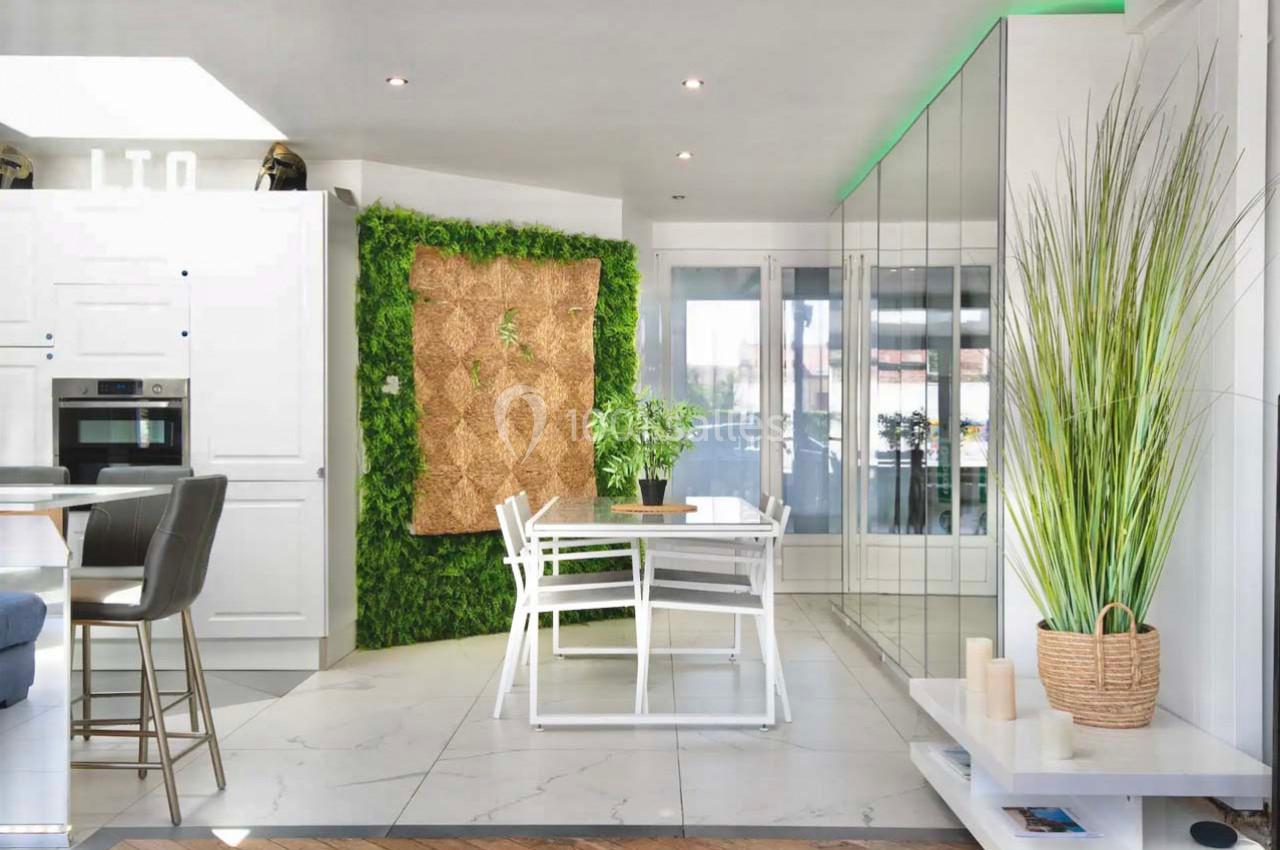 Cuisine moderne avec coin repas, mur végétal, mobilier blanc, et décoration minimaliste dans un espace lumineux.