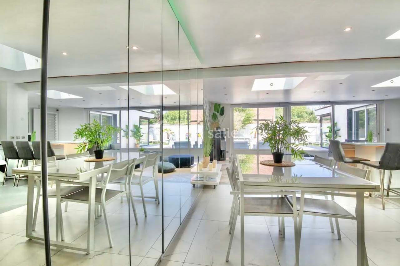 Salle à manger moderne avec table en verre, chaises blanches, plantes décoratives et grandes baies vitrées.