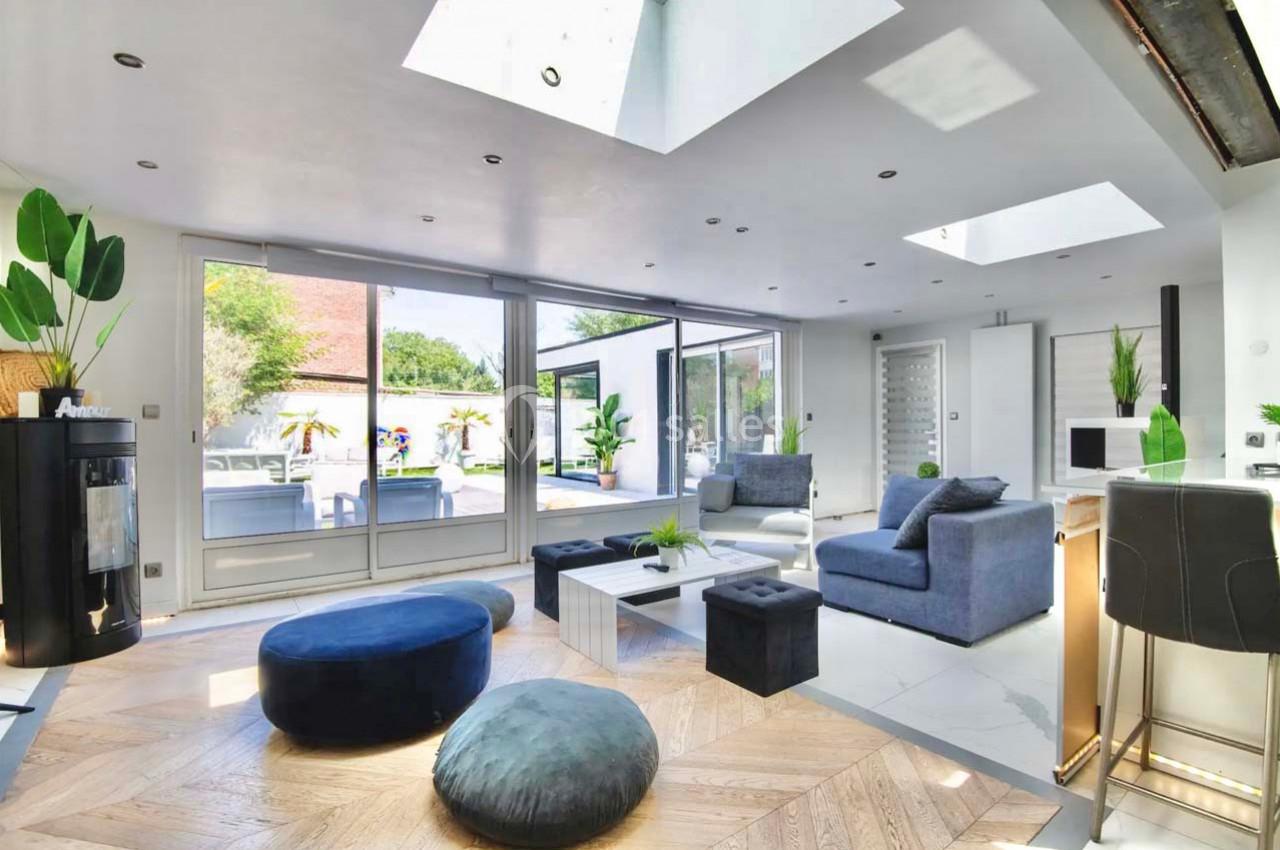 Salon lumineux avec baies vitrées, mobilier moderne, parquet en bois clair et vue sur une terrasse extérieure.