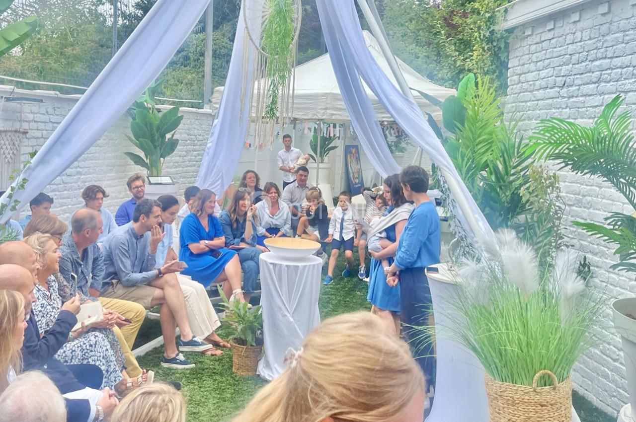 Un groupe de personnes assises dans un jardin décoré, assistant à une cérémonie sous un voile blanc.