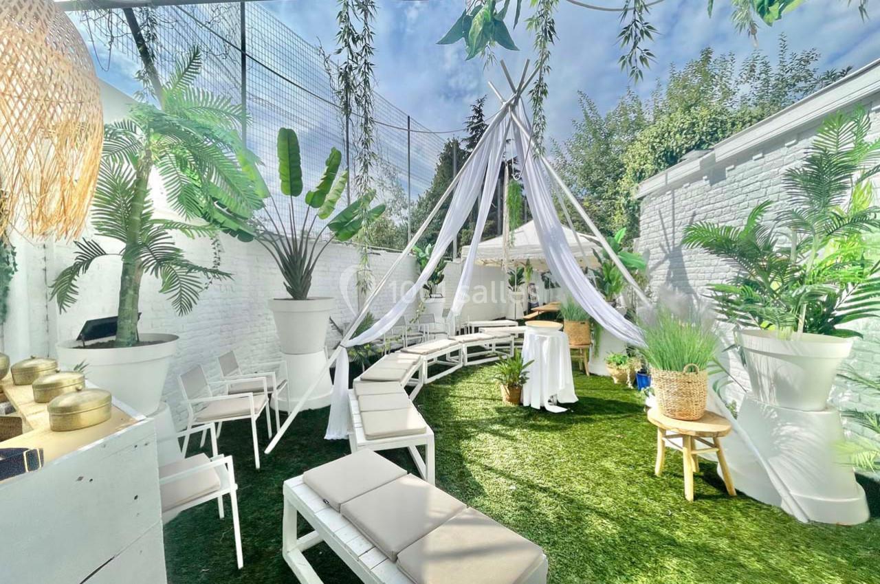 Espace extérieur lumineux avec bancs blancs, plantes en pots et voilages suspendus sous un ciel dégagé.