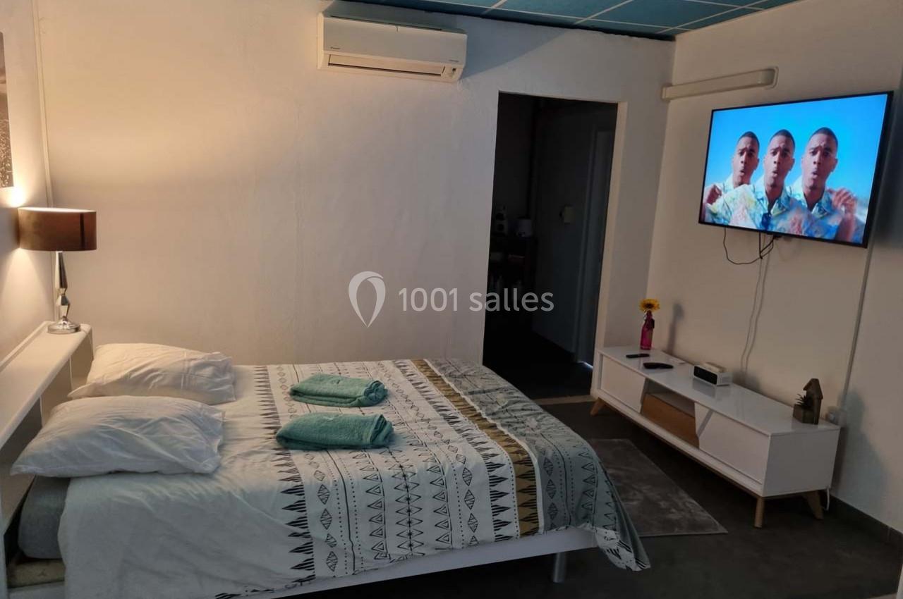 Chambre lumineuse avec lit double, linge plié, télévision murale allumée et mobilier moderne.