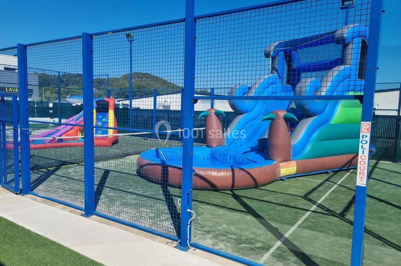 Structures gonflables colorées installées sur un terrain clôturé, avec un sol en gazon synthétique.