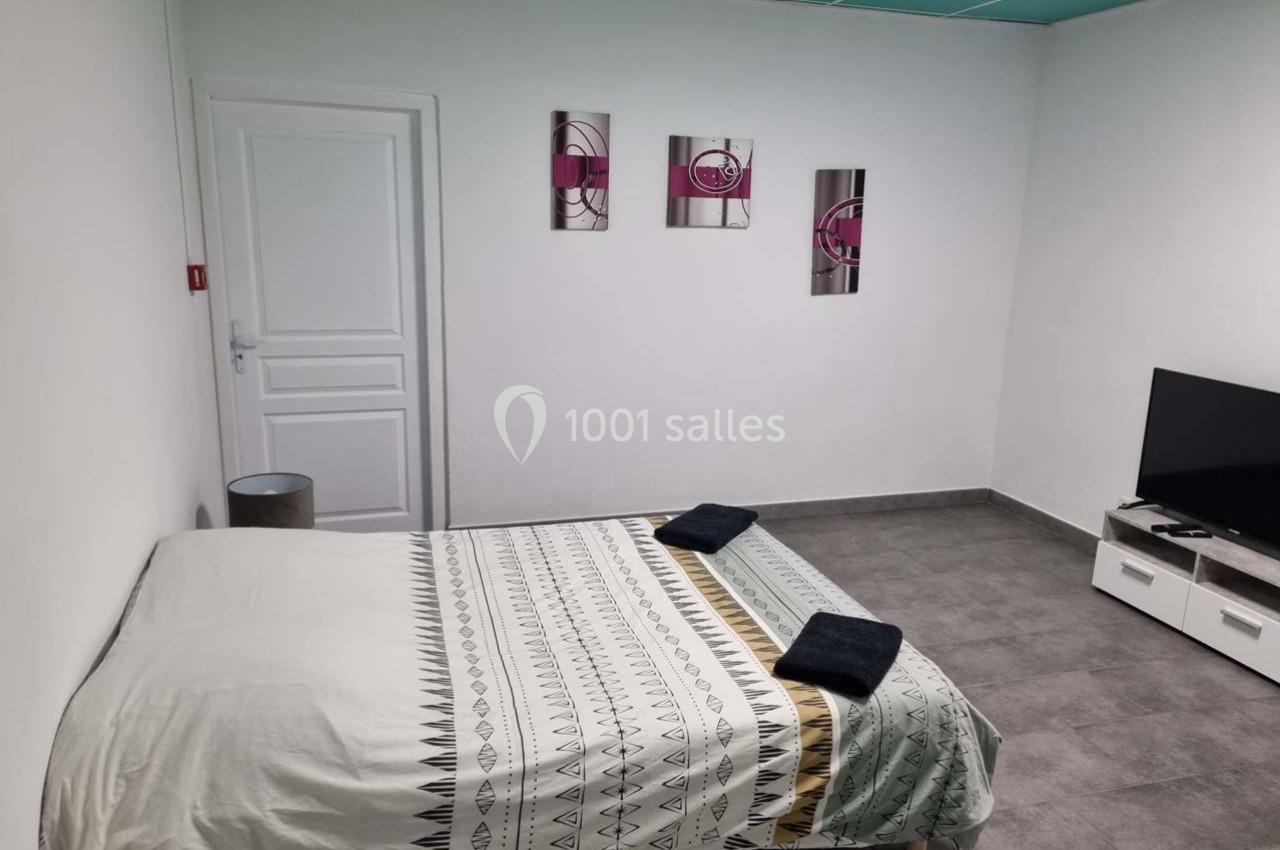 Chambre avec lit double, télévision, sol en carrelage gris, murs blancs et décoration murale moderne.