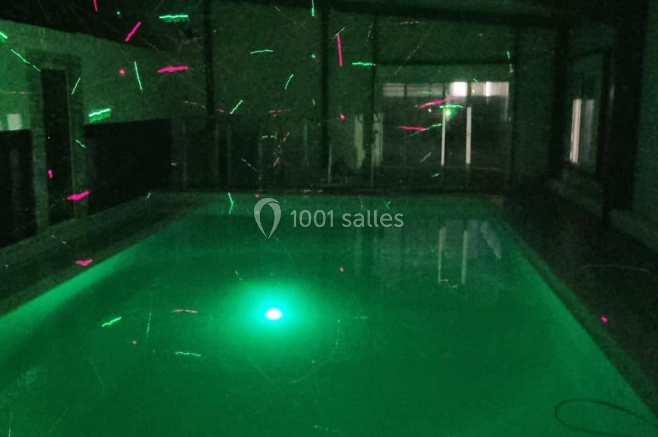 Piscine intérieure éclairée par des lumières vertes et roses dans une ambiance sombre.