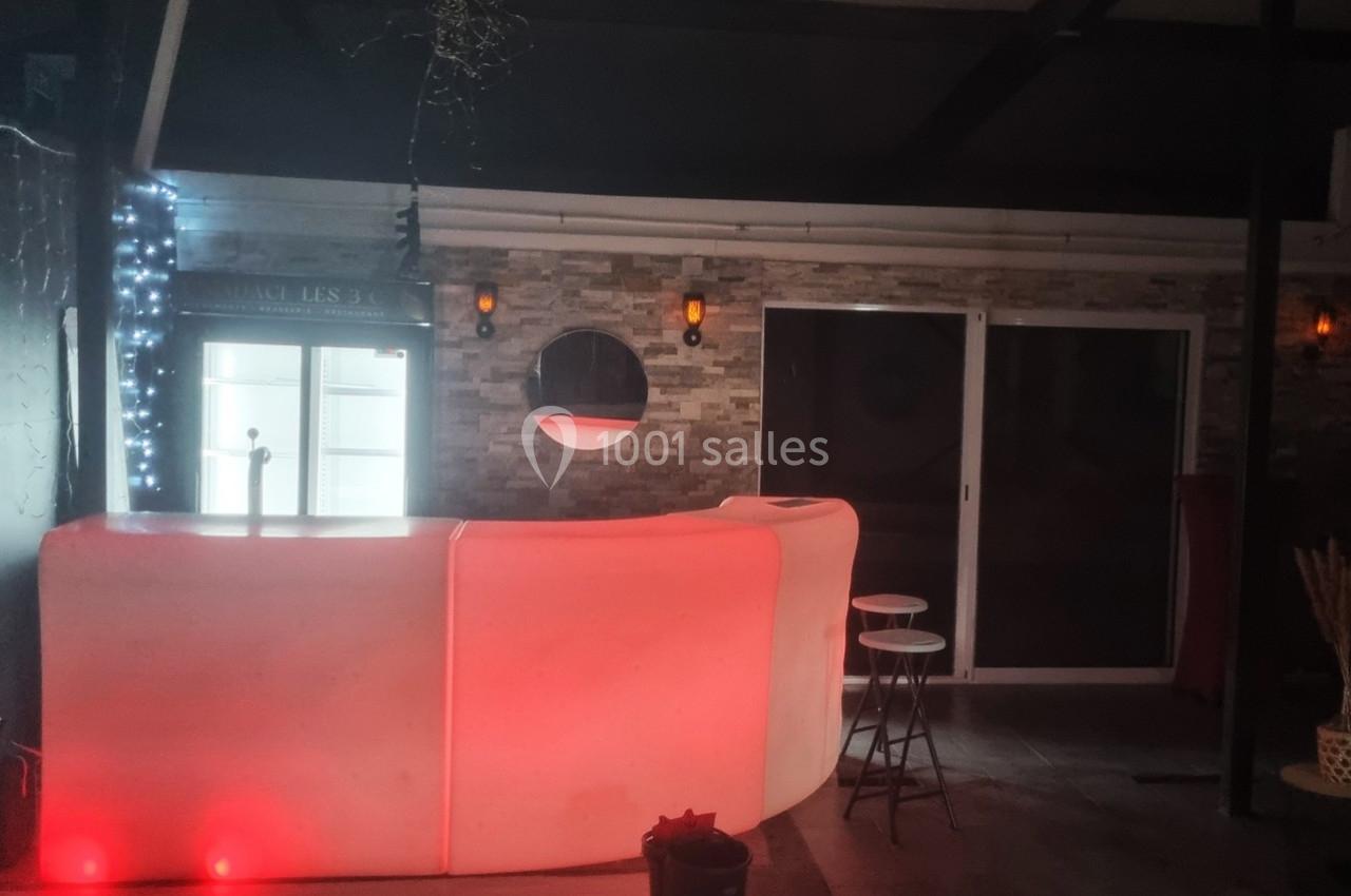 Comptoir lumineux rouge dans un espace intérieur sombre avec murs en pierre, tabourets et éclairages muraux.